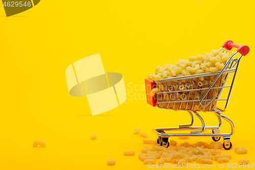 Image of A grocery cart to the top is filled with pasta on a bright orange background, some pasta is lying next to the cart