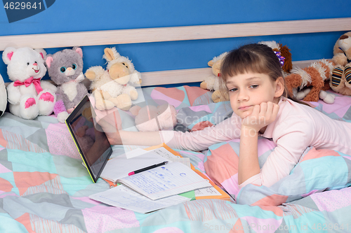 Image of Schoolgirl does homework while lying in bed with a tablet