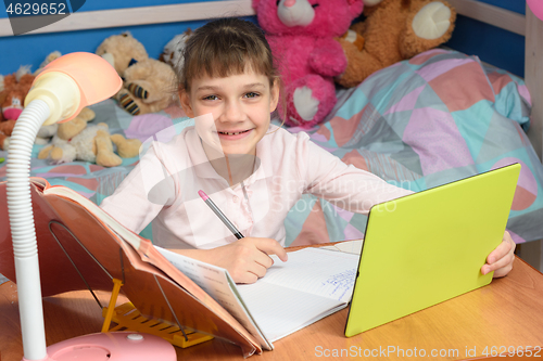 Image of Cheerful girl doing homework using tablet computer