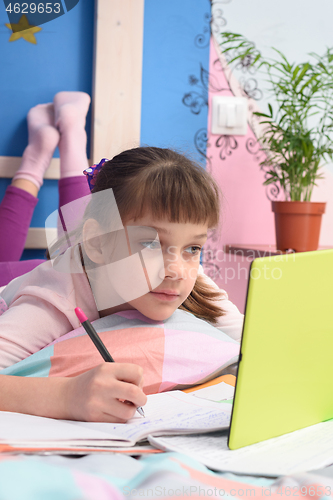 Image of Schoolgirl watches video tutorials in a tablet computer and lies in bed