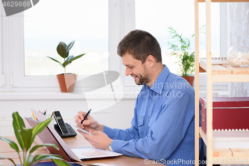 Image of Successful office worker with a smile makes an entry in a notebook