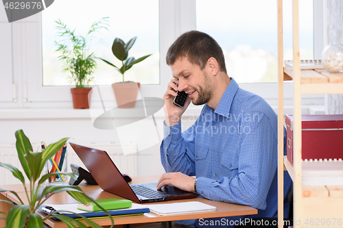 Image of Young businessman talking on the phone in the office and working in a laptop