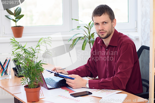 Image of Pensive office specialist sits at a table in the office and looked into the frame