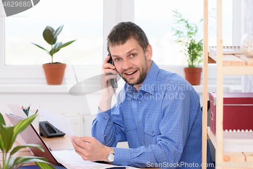 Image of Businessman talking on the phone at his workplace and looking in the frame.