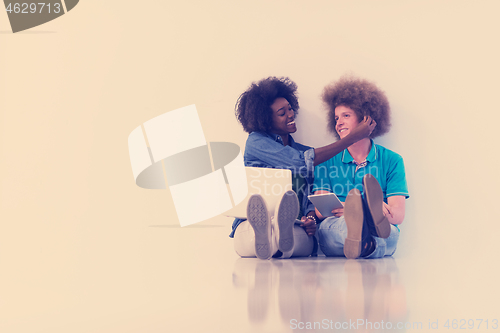 Image of multiethnic couple sitting on the floor with a laptop and tablet