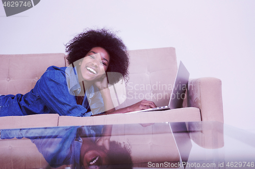 Image of African American woman using laptop on sofa
