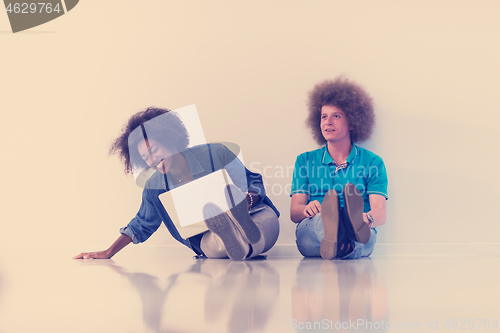 Image of multiethnic couple sitting on the floor with a laptop and tablet