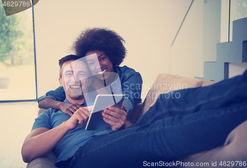 Image of multiethnic couple relaxing at  home with tablet computers