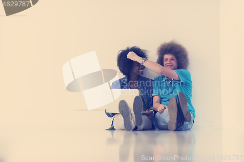 Image of multiethnic couple sitting on the floor with a laptop and tablet