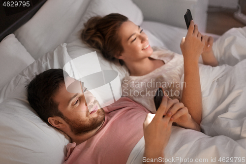 Image of couple using smartphones in bed at night