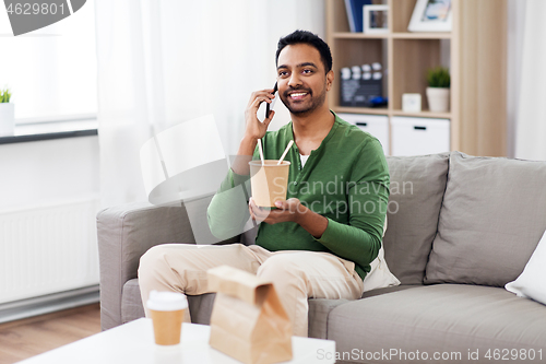 Image of smiling indian man eating takeaway food at home