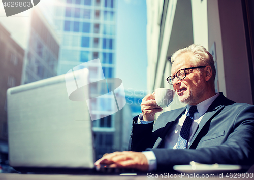 Image of senior businessman with laptop drinking coffee