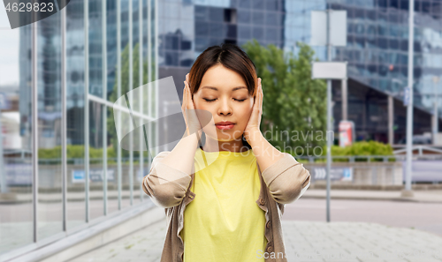 Image of asian woman closing ears by hands on city street