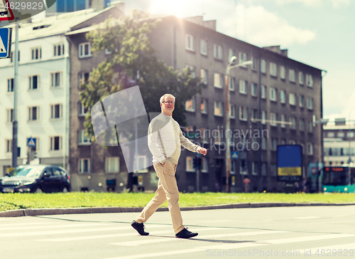 Image of senior man walking along city crosswalk