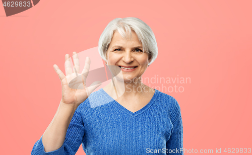 Image of smiling senior woman showing palm or five fingers