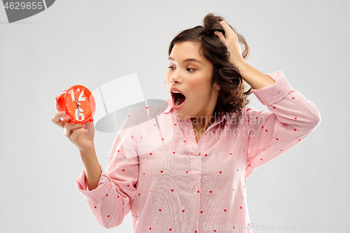 Image of shocked young woman in pajama with alarm clock