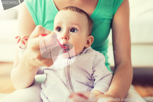 Image of mother with spoon feeding little baby at home