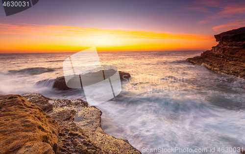 Image of Sunrise over the ccean with some foreground rocks of eroded sand