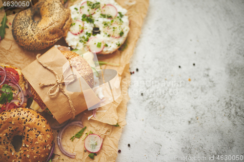 Image of Bagels with ham, cream cheese, hummus, radish wrapped in brown baking paper ready for take away