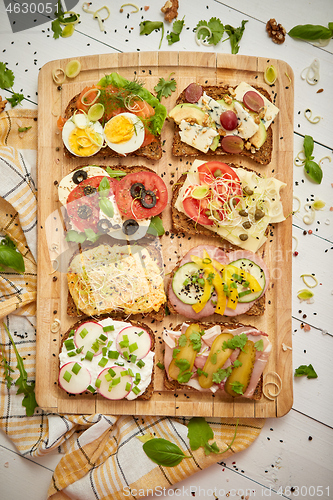 Image of Colorful, different kinds sandwiches served on wooden chopping board. Vegetable toppings