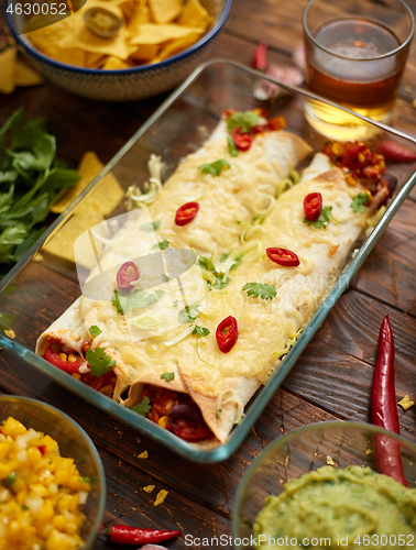 Image of Vegetable Burritos served in glass heatproof dish. With salsa, guacamole, nachos and ingredients