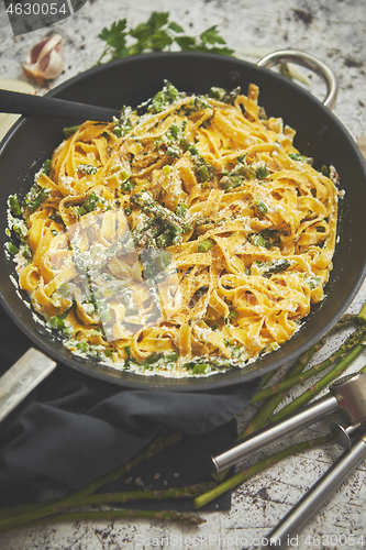 Image of Tagliatelle pasta with ricotta cheese sauce and asparagus served on a black iron pan