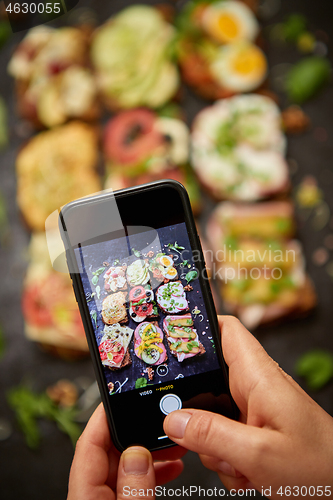 Image of Woman making a photo with a smartphone of assortment of home made sandwiches with various toppings