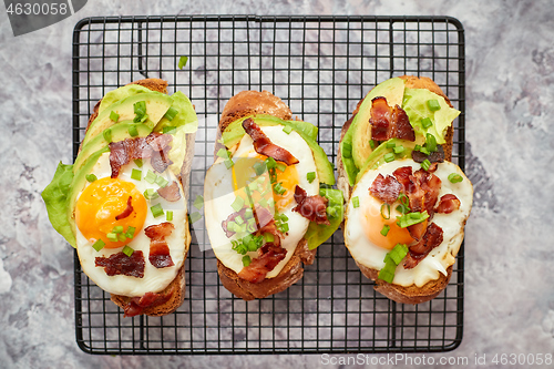 Image of Tasty delicious homemade toasts with fried egg, bacon, avocado, lettuce and chive. Served on grill