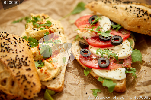 Image of Two delicious sandwiches with hummus, tomato, mozarella cheese, herbs and olives