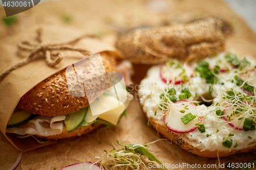 Image of Bagels with ham, cream cheese, hummus, radish wrapped in brown baking paper ready for take away