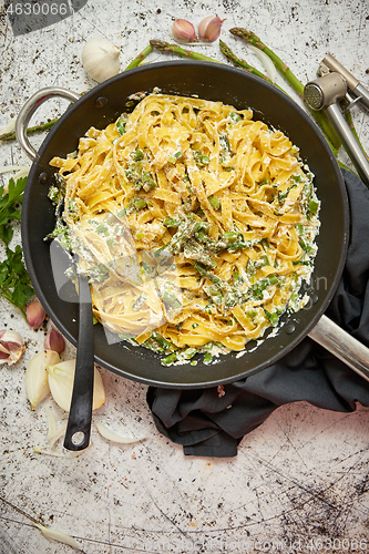 Image of Homemade tagliatelle pasta with ricotta cheese creamy sauce and fresh asparagus served on a iron pan