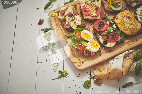 Image of Tasty, homemade small sandwiches with various ingredients served on wooden chopping board