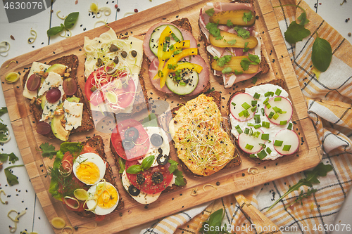 Image of Tasty, homemade small sandwiches with various ingredients served on wooden chopping board