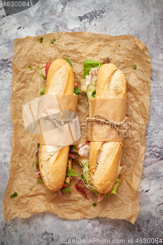 Image of Sandwiches with ham, fresh vegetables and herbs served on brown baking paper over concrete backdrop