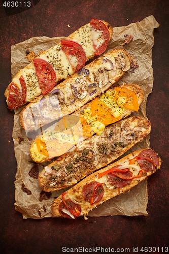 Image of Assortment of various toppings baked sandwiches. With melted cheese, vegetables, tuna, olives spices