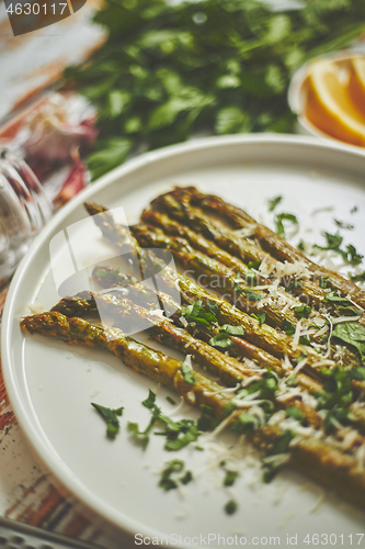 Image of Delicious roasted asparagus served on white ceramic plate. With parmesan cheese, parsley and lemon.