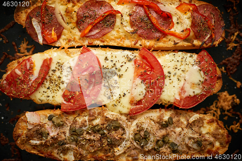 Image of Long baguettes pizza sandwiches with tuna, mushrooms, tomatoes and cheese on a metal baking tray