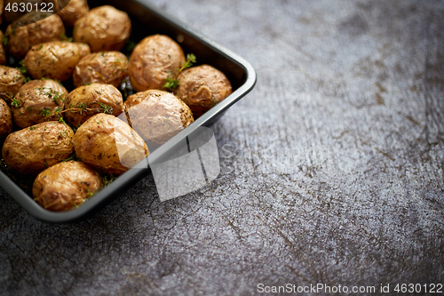 Image of Homemade roasted whole potatoes in jackets. With butter, rosemary and thyme. Served in metallic dish