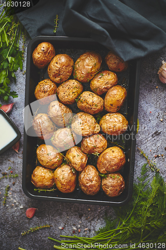 Image of Tasty fresh homemade baked potatoes served on a metal tray. With various herbs, butter, garlic, salt