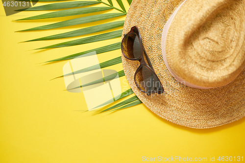 Image of Straw hat, green palm leaf and sunglasses on yellow backdrop. Su