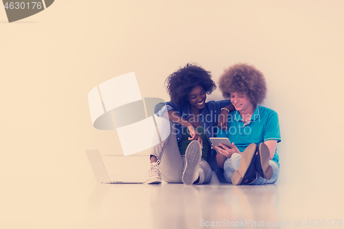 Image of multiethnic couple sitting on the floor with a laptop and tablet