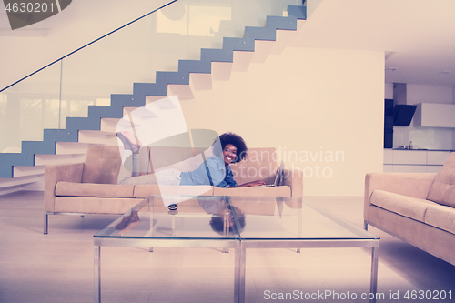 Image of African American woman using laptop on sofa