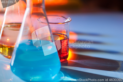 Image of Illuminated laboratory flask filed with colorful chemical solutions with shadows on the table. Laboratory, science, chemistry... consept.