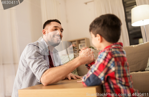 Image of happy father and little son arm wrestling at home