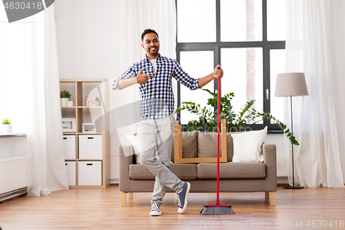Image of smiling indian man with broom cleaning at home