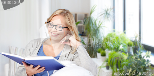 Image of smiling woman reading book and sitting on couch