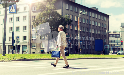 Image of senior man with shopping bags walking on crosswalk