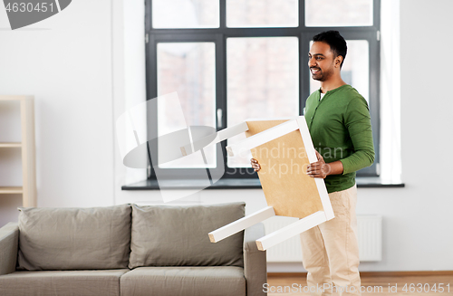 Image of happy indian man holding coffee table at home