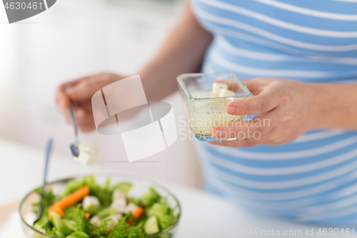 Image of close up of pregnant woman cooking salad at home