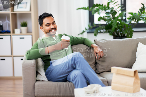 Image of happy indian man drinking takeaway coffee at home